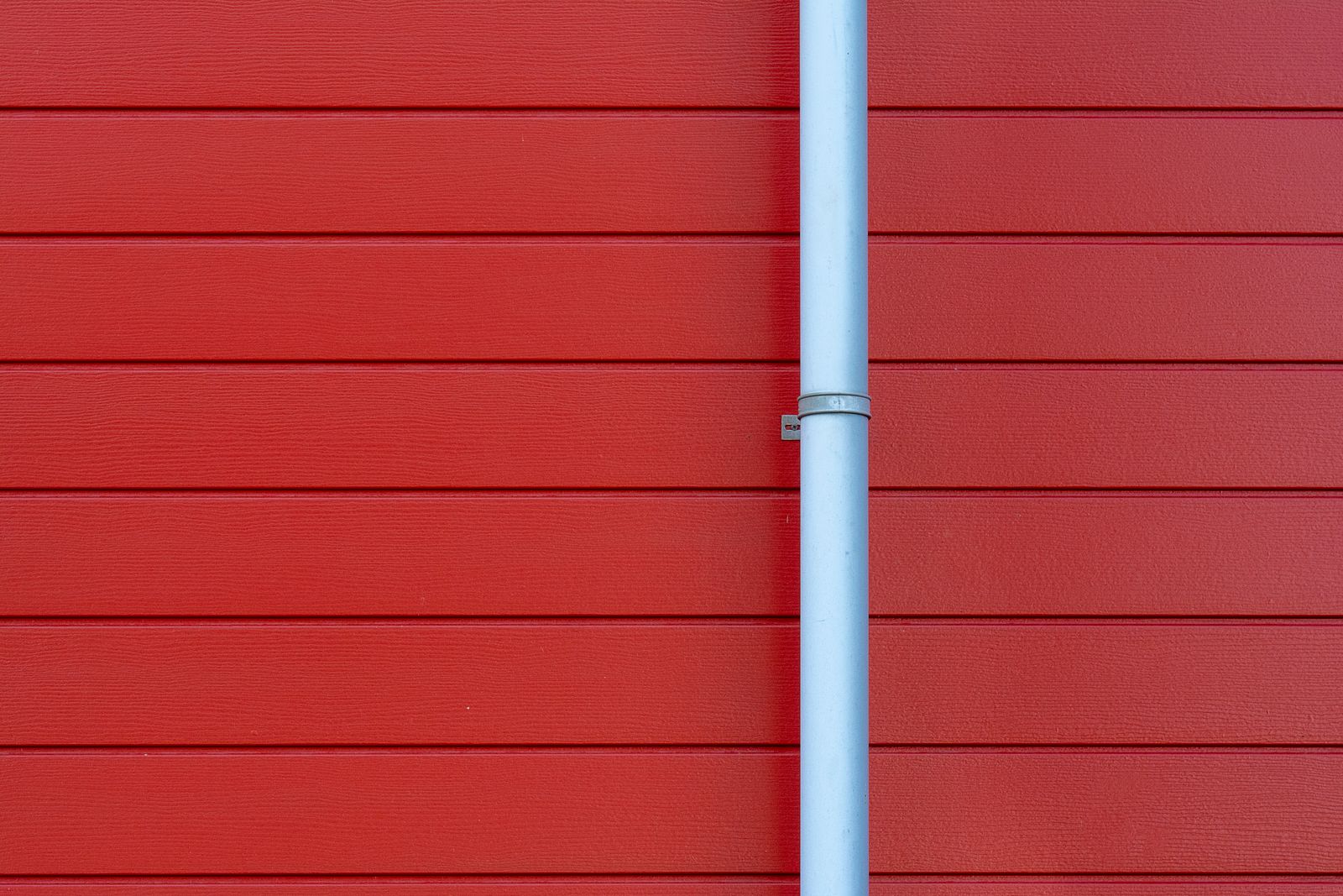 Light gray downspout mounted against red siding